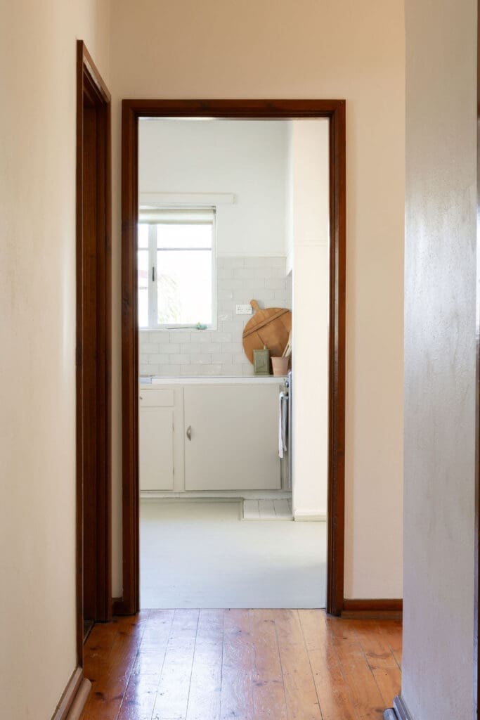 Hallway with original timber floorboards leading to the kitchen of a staged red brick cottage in O’Connor, Canberra